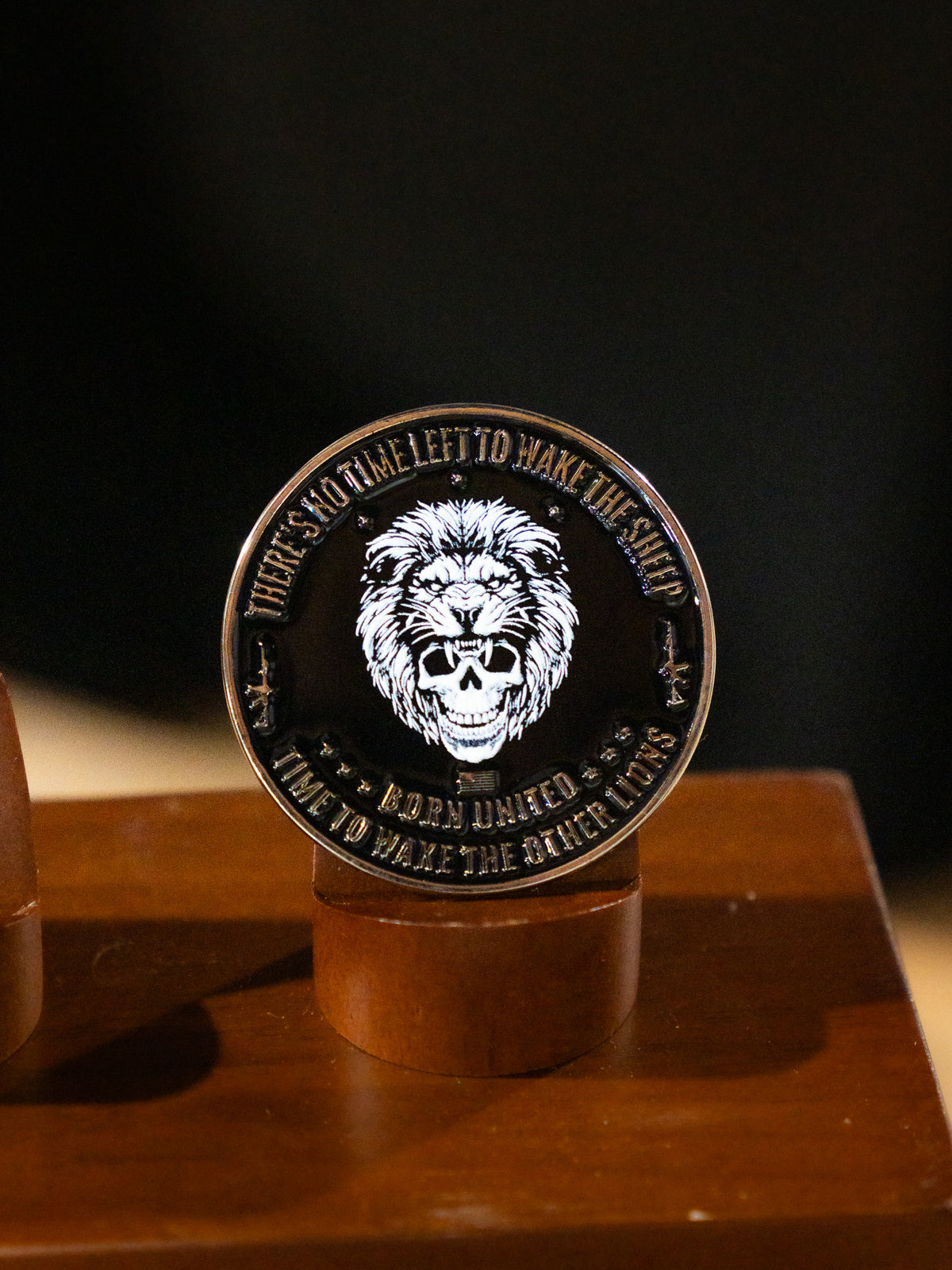The Born United Private Label Waking Lions Challenge Coin displays a roaring lion and the quote "THERE'S NO TIME LEFT TO WAKE THE SHEEP, IT'S TIME TO WAKE THE OTHER LIONS," shown upright on a wooden surface.