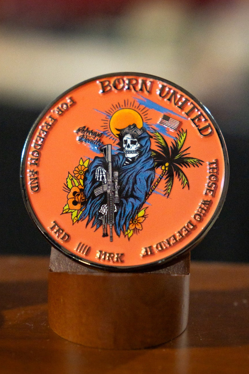 The Always Deadly Challenge Coin by Born United Private Label is a round, orange coin showing a skeleton in a blue cloak with a rifle, plus palm tree, sun, and smoke. The edge reads: "BORN UNITED, FOR THOSE OF KIND, FOR THOSE OF DEVASTATION—Always Deadly.