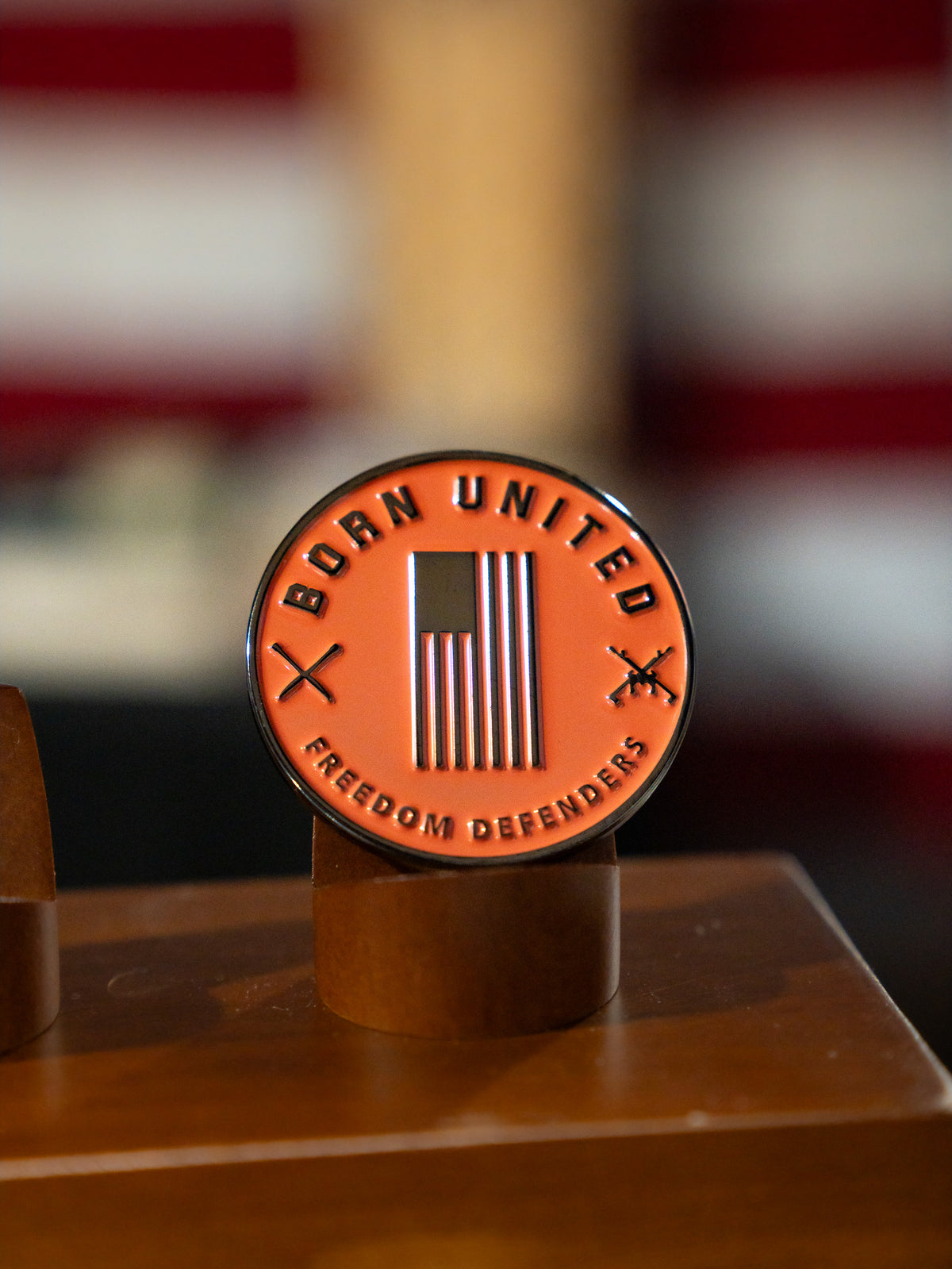 The Born United Private Label "Always Deadly Challenge Coin" features an American flag, “BORN UNITED” on top, “FREEDOM DEFENDERS” below, two crossed rifles, and the phrase Always Deadly. Displayed on a wooden stand.