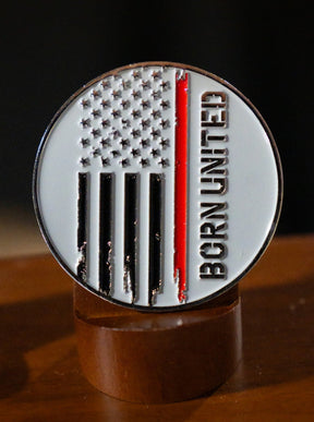 The Born United Private Label Red Line Flag Challenge Coin features a round design with black and white stripes, one bold red stripe for support, and "BORN UNITED" on the right side—a perfect fan collectible displayed on wood.