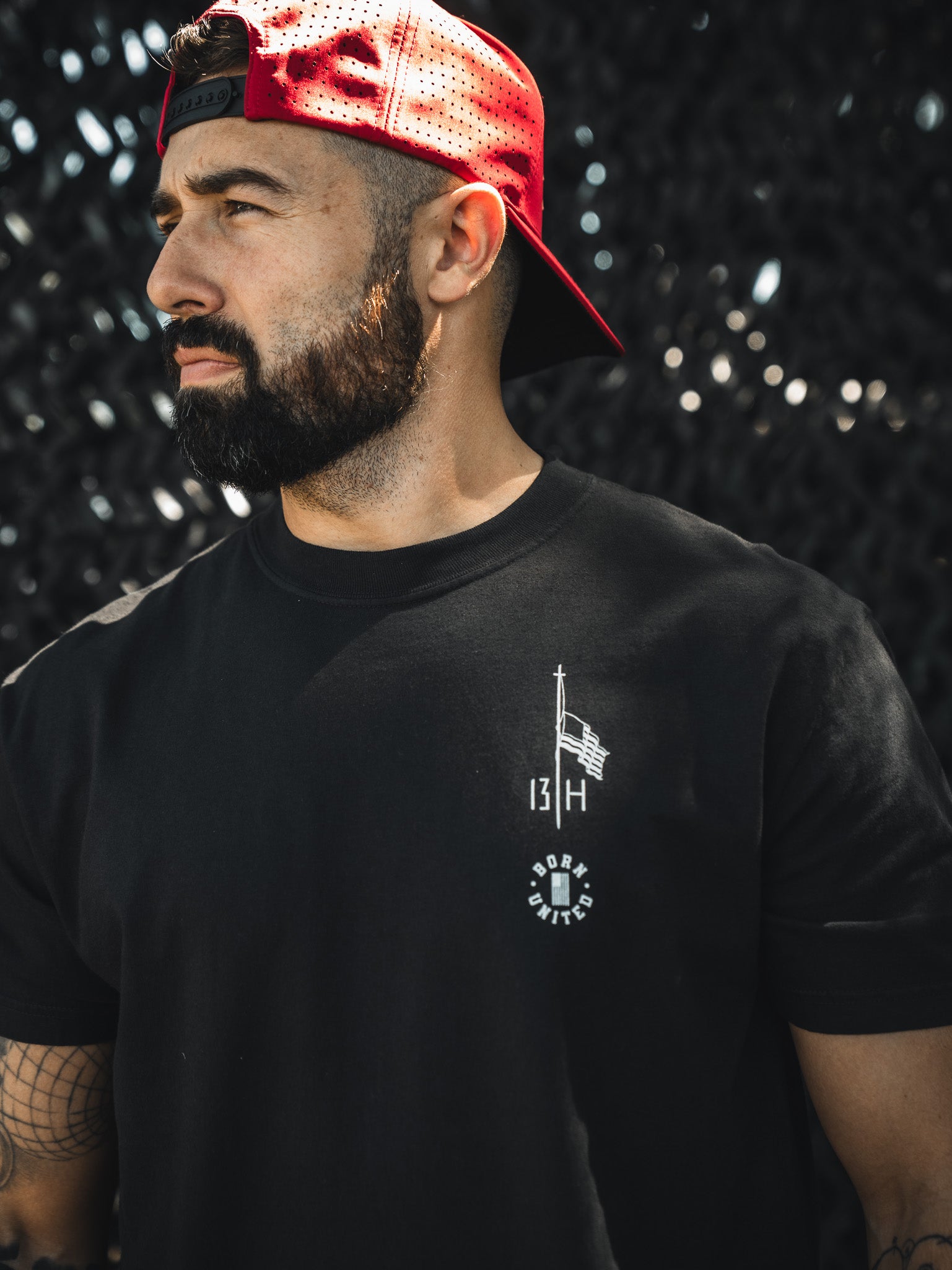 A bearded man in a backward red cap and a Born United Private Label "Live Like Charlie" tee stands before a dark textured background, gazing to the side.