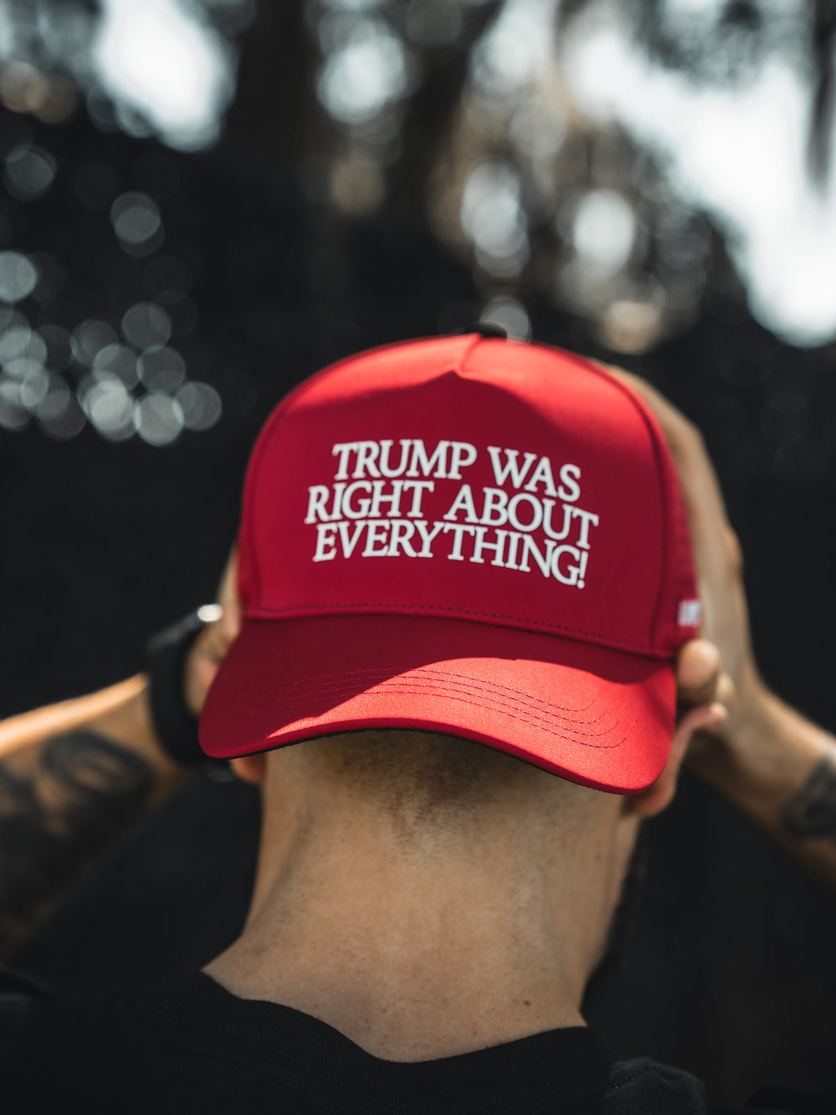 A person wearing the Born United Premium Snapback - Trump Was Right by Born United Private Label, featuring white text that reads "TRUMP WAS RIGHT ABOUT EVERYTHING!", is facing away from the camera and holding the back of their head.
