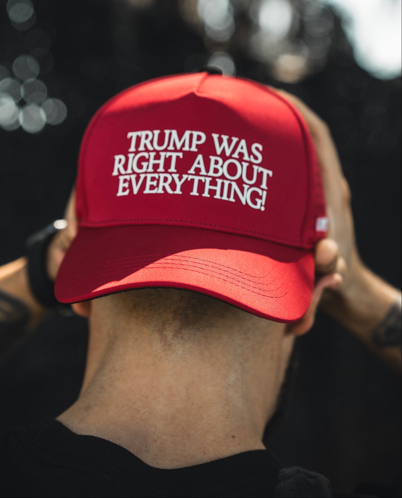 A person wearing the Born United Premium Snapback - Trump Was Right by Born United Private Label, featuring white text that reads "TRUMP WAS RIGHT ABOUT EVERYTHING!", is facing away from the camera and holding the back of their head.