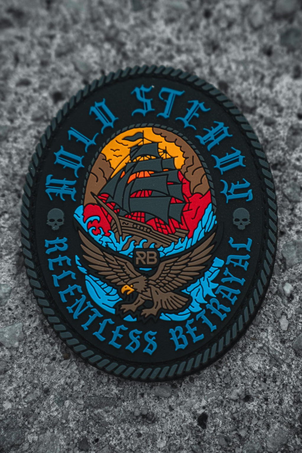 The Hold Steady Patch by Relentless Betrayal is a 3x3" round patch featuring a sailing ship, eagle, skulls, and rope edging in bold blue, red, and yellow with "HOLD STEADY RELENTLESS BETRAYAL" around the border.