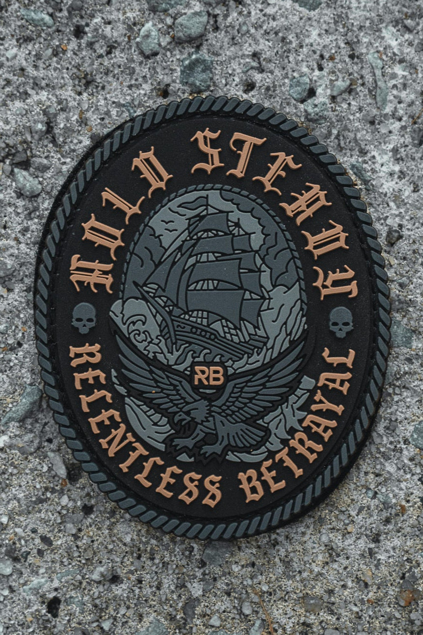The Hold Steady Ghost Patch by Relentless Betrayal is a 3" 3D PVC patch with a sailing ship and eagle design, “HOLD STEADY” on top and “RELENTLESS BETRAYAL” below. It features Velcro backing and is shown on rough gray concrete.