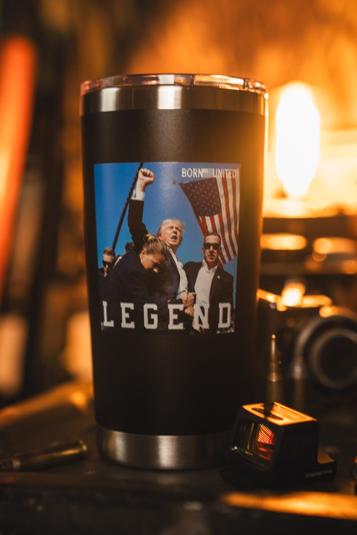 The Born United Private Label Forever Legend Tumbler - 20oz is a stainless steel travel mug featuring an image of a man holding an American flag with "LEGEND" below, photographed in a warmly lit room with blurred background.