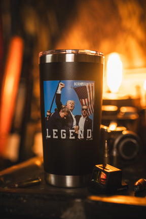 The Born United Private Label Forever Legend Tumbler - 20oz is a stainless steel travel mug featuring an image of a man holding an American flag with "LEGEND" below, photographed in a warmly lit room with blurred background.