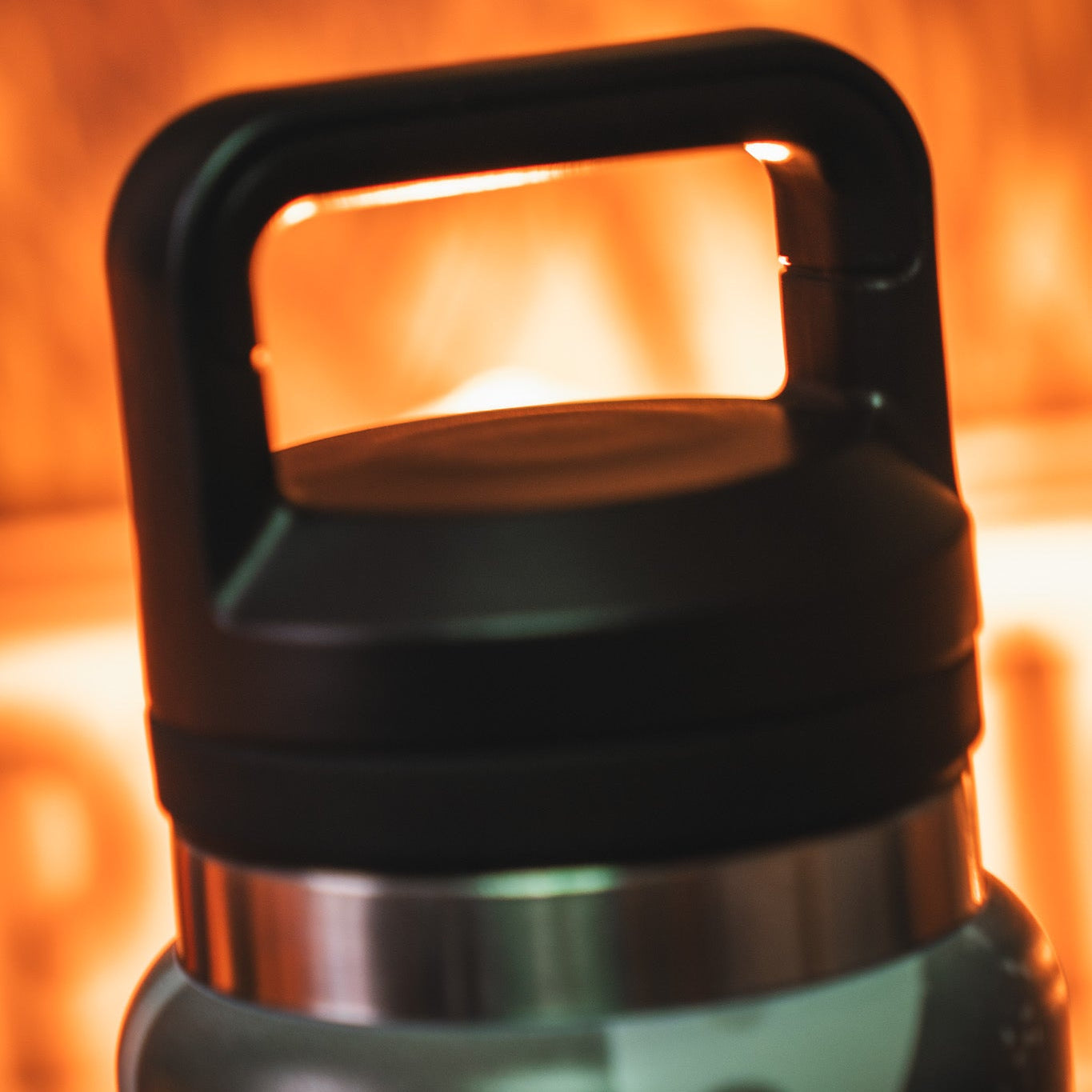 Close-up of the leak proof lid with handle on the Mucker Bucket Duck Jug—Duck Camo Water Bottle (26oz), black and silver stainless steel, set against a warm, blurred background.