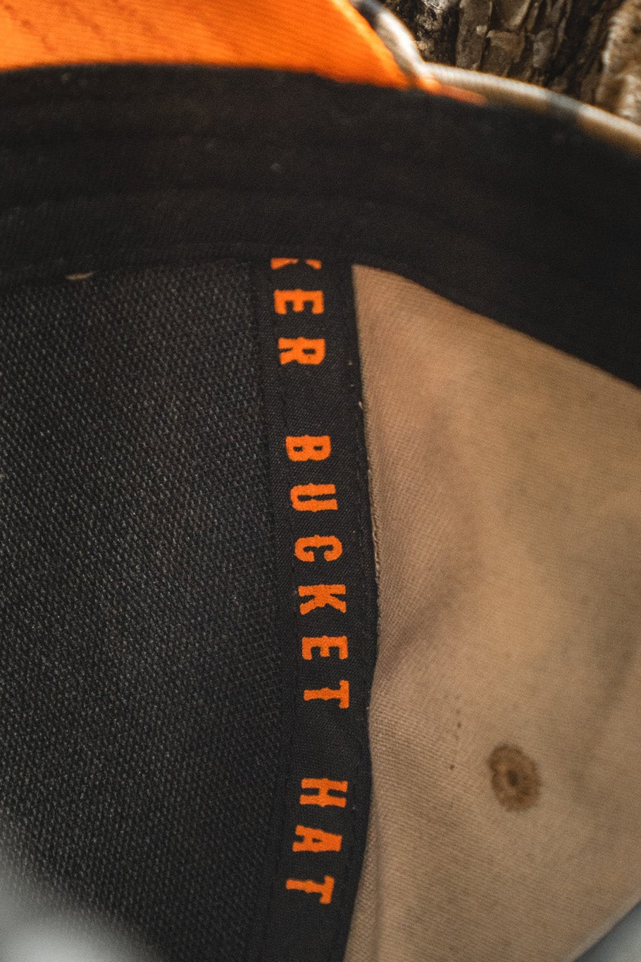 Close-up of the inside of the Mallard Life Deadwood Camo Bucket by Mucker Bucket, showing black and tan deadwood camo fabric with "Mucker Bucket" in orange lettering on the inner band.