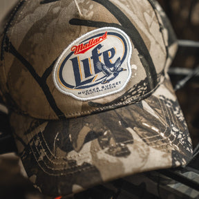 The Mallard Life Deadwood Camo Bucket by My Store is a camo snapback hat with a patch that reads "Mallard Life Mucker Bucket Southern Goods," including a flying duck graphic and brown-tan accents.