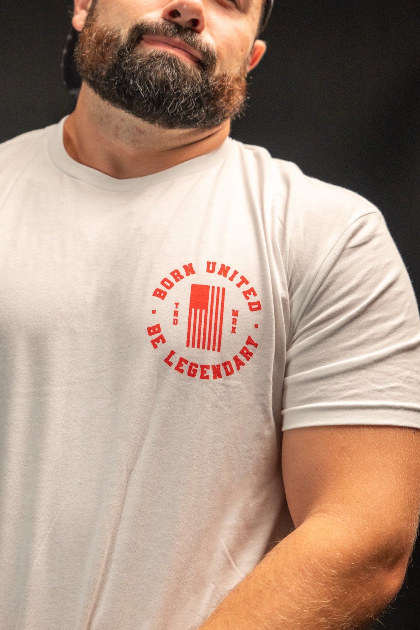 A bearded, capped man wearing a Born United Private Label t-shirt with Born United, Be Legendary in red text poses with a raised eyebrow against a black background, channeling the timeless charm of Legends - Dukes of Hazzard.