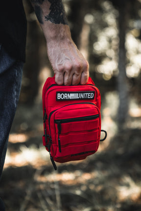 A person holds the Red Reaper Tactical Sling-Pac (4L) by Born United Private Label, featuring multiple zippered compartments and a signature patch—ideal for concealed carry or use as a compact tactical sling bag outdoors.