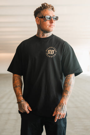 A tattooed man wearing sunglasses and a Relentless Betrayal Never Surrender Premium Oversized Ghost T-Shirt with a white chest graphic stands in a modern, sunlit indoor space.