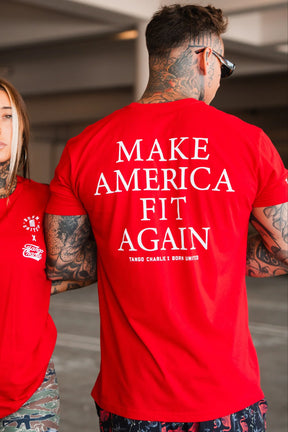 Wearing a bold red Make America Fit Again - Tee from Tango Charlie Apparel, a man stands in a parking garage. His tattoos and sunglasses complete his standout look as he promotes health, wellness, and preventive care.