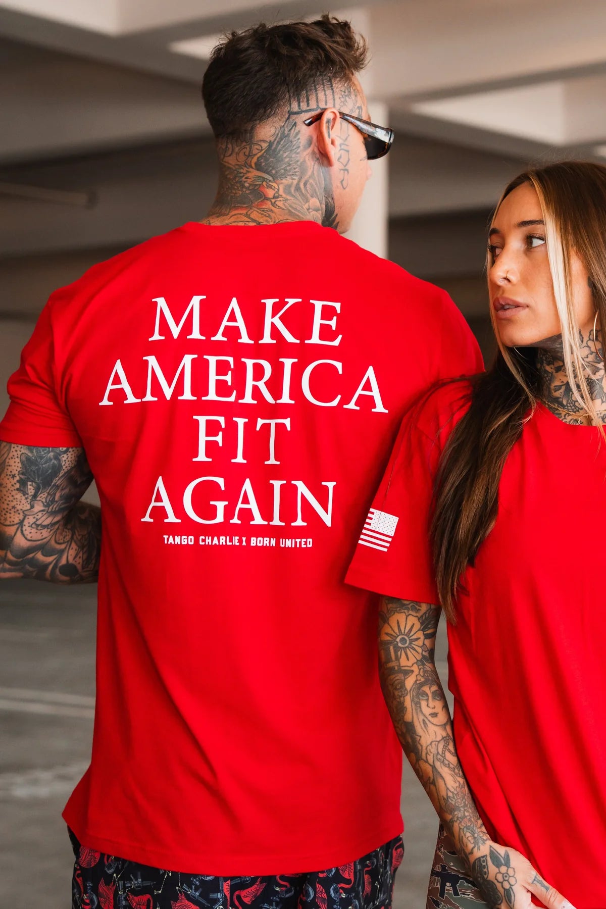 Two tattooed individuals wear Tango Charlie Apparel's "Make America Fit Again" tee and a red shirt with an American flag patch, celebrating preventive care and wellness.