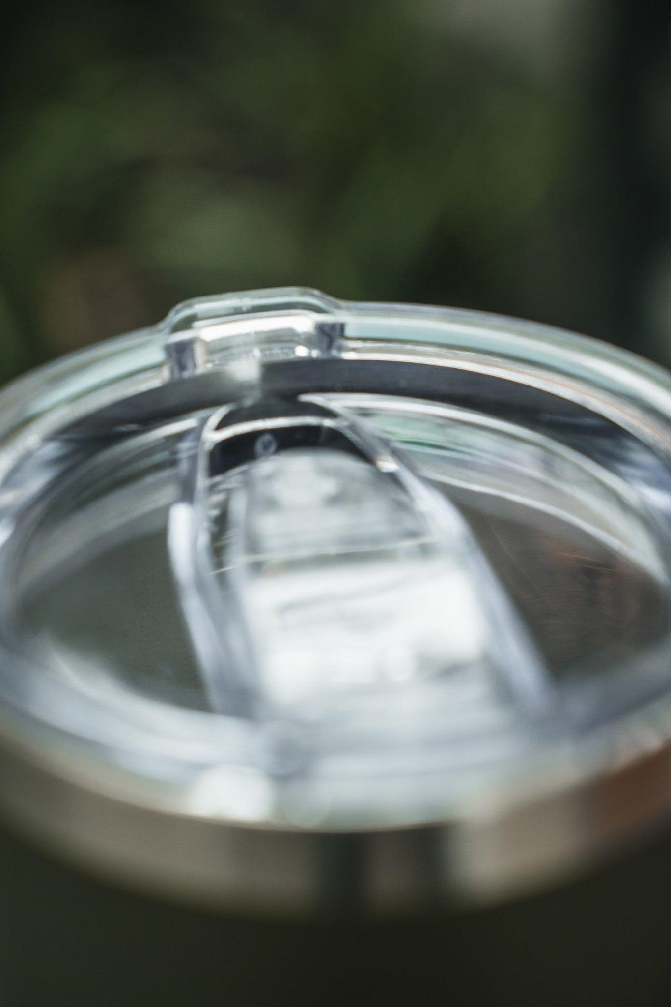 A clear plastic sliding lid tops the stainless steel 20oz Triggered Tumbler by Born United Private Label, shown against a soft green backdrop.