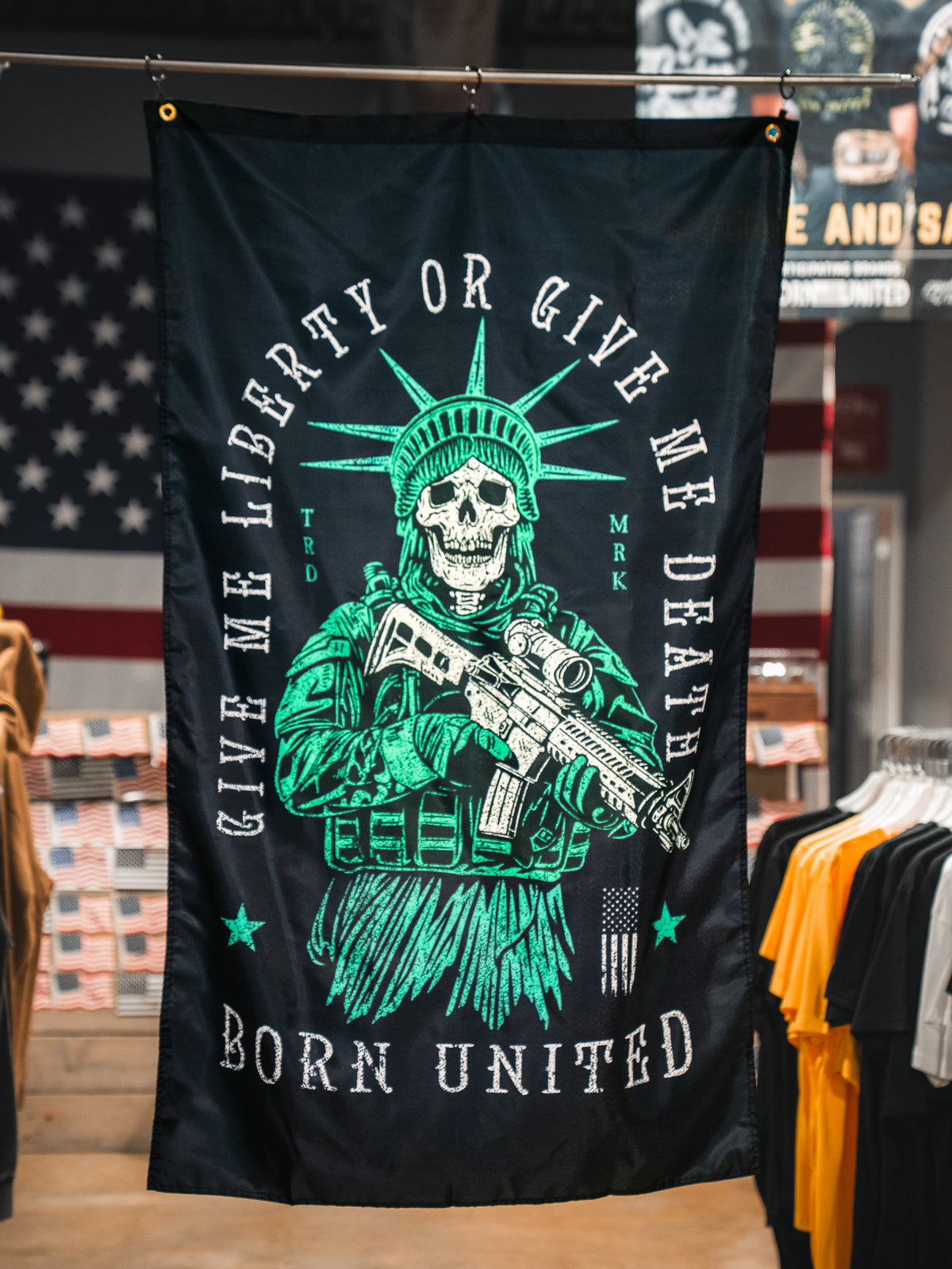 The Liberty or Death Flag by Born United Private Label features a skeleton Statue of Liberty with a rifle and the phrases "Give me liberty or give me death" and "Born United" on a dark background, inspired by American revolutionary flags.