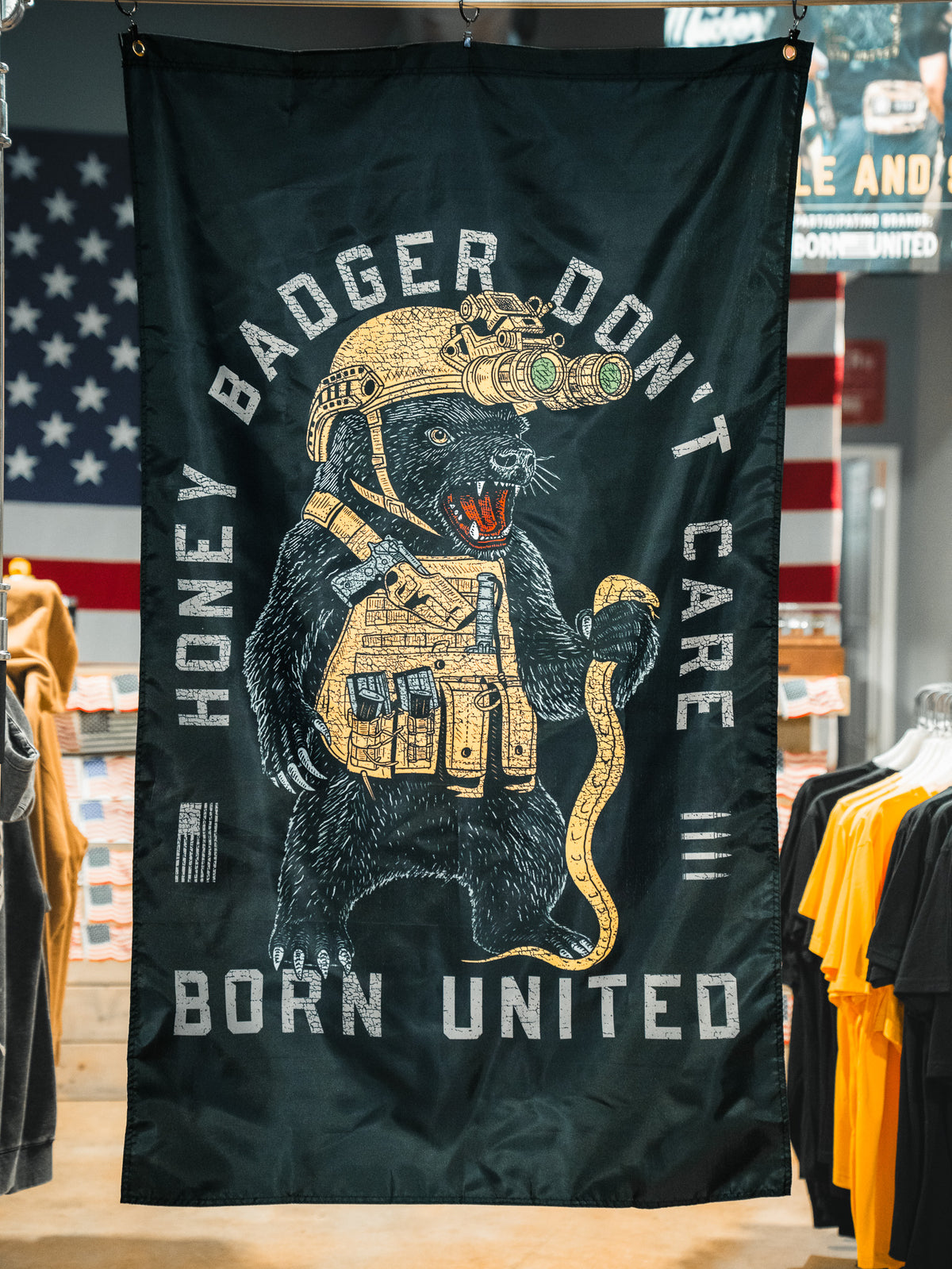 The Honey Badgerin' Flag by Born United Private Label features a fierce honey badger in tactical gear with night vision goggles and snake, "HONEY BADGER DONT CARE" above and "BORN UNITED" below, plus an American flag backdrop. Made of durable polyester.