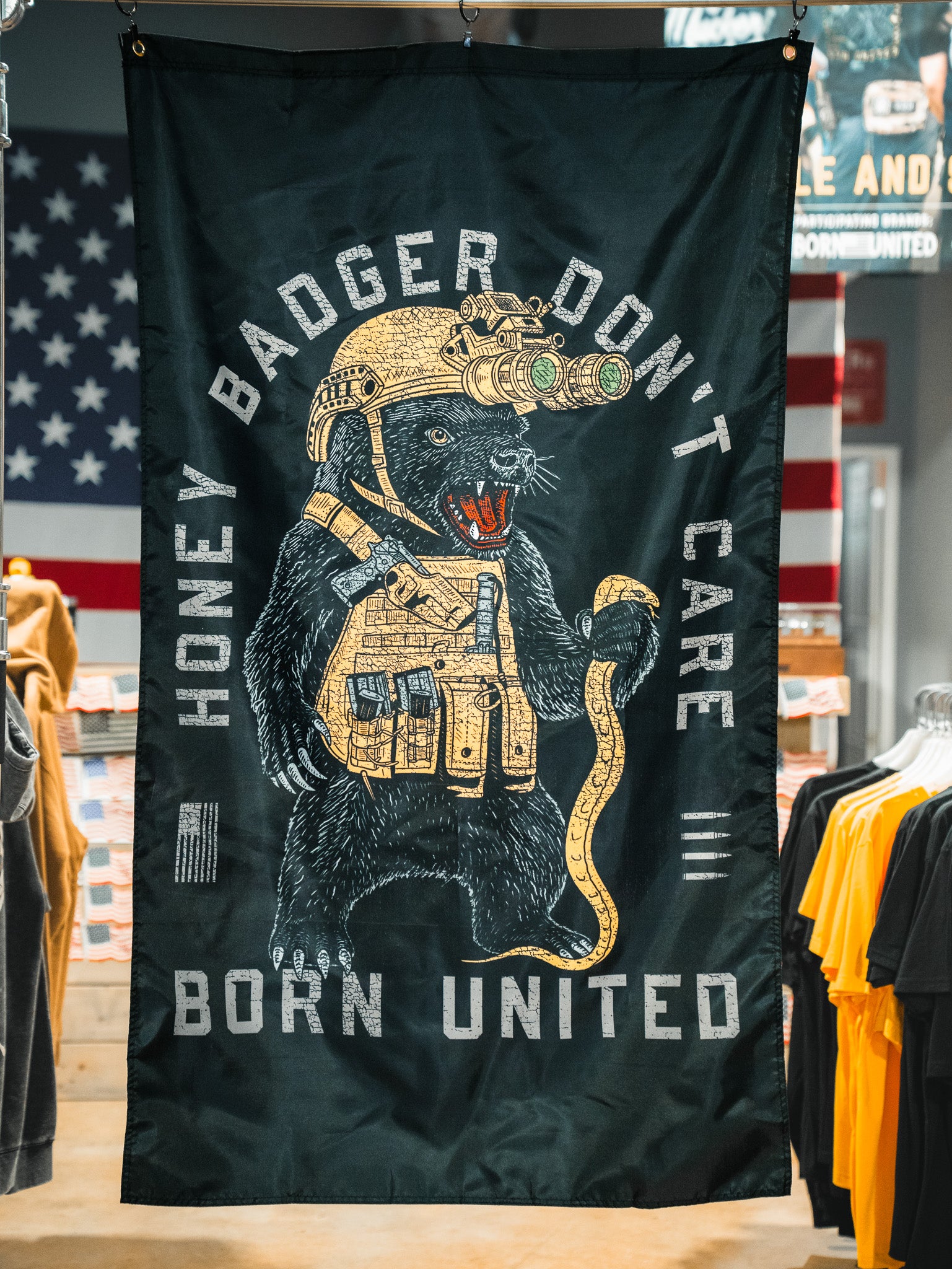 The Honey Badgerin' Flag by Born United Private Label features a fierce honey badger in tactical gear with night vision goggles and snake, "HONEY BADGER DONT CARE" above and "BORN UNITED" below, plus an American flag backdrop. Made of durable polyester.