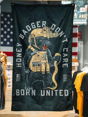 The Honey Badgerin' Flag by Born United Private Label features a fierce honey badger in tactical gear with night vision goggles and snake, "HONEY BADGER DONT CARE" above and "BORN UNITED" below, plus an American flag backdrop. Made of durable polyester.