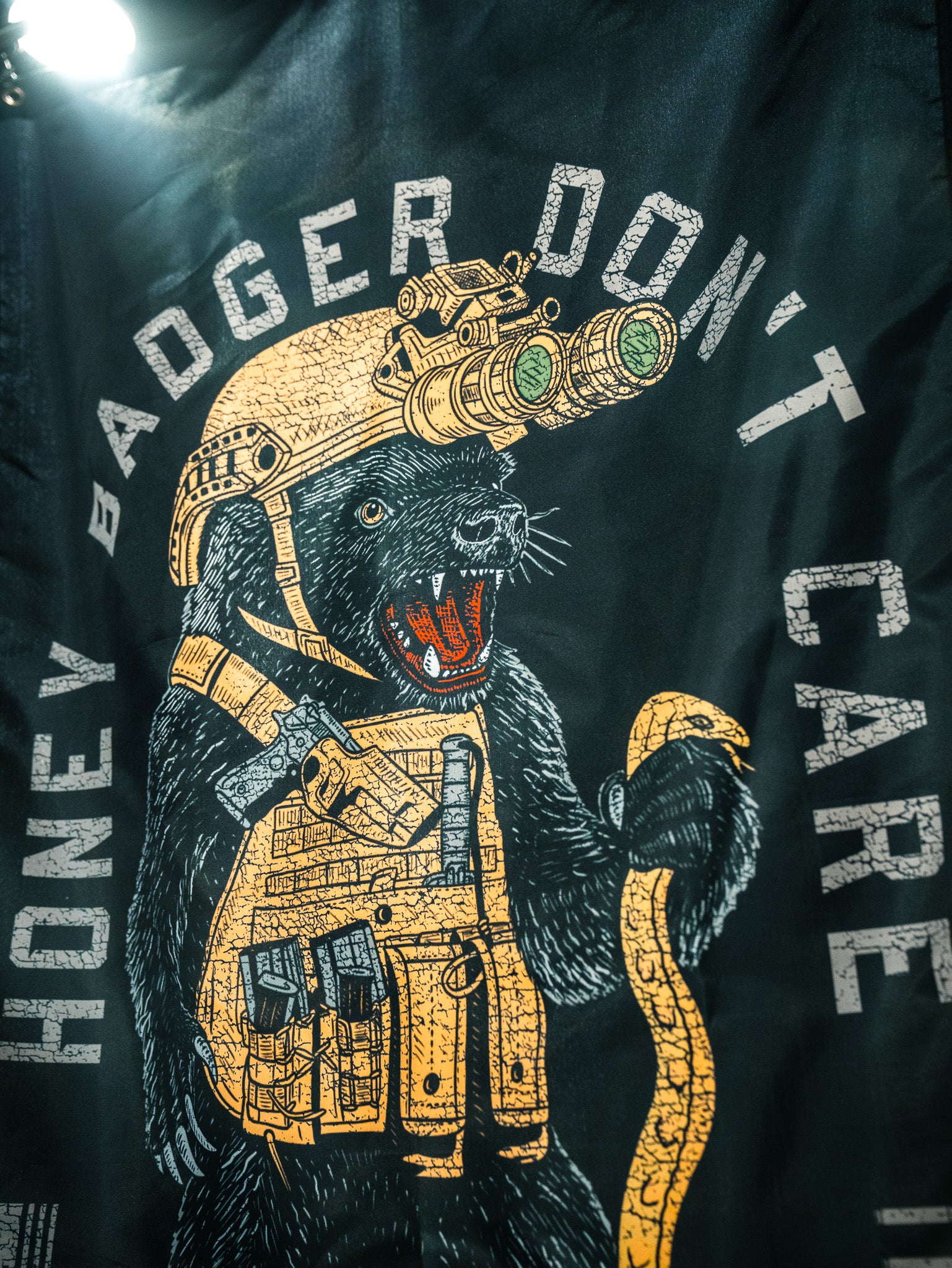 Illustration of a fierce honey badger in tactical gear with night vision goggles, holding a snake. The flag reads "HONEY BADGER DONT CARE." Born United Private Label's Honey Badgerin' Flag—perfect for bold collections or durable display.