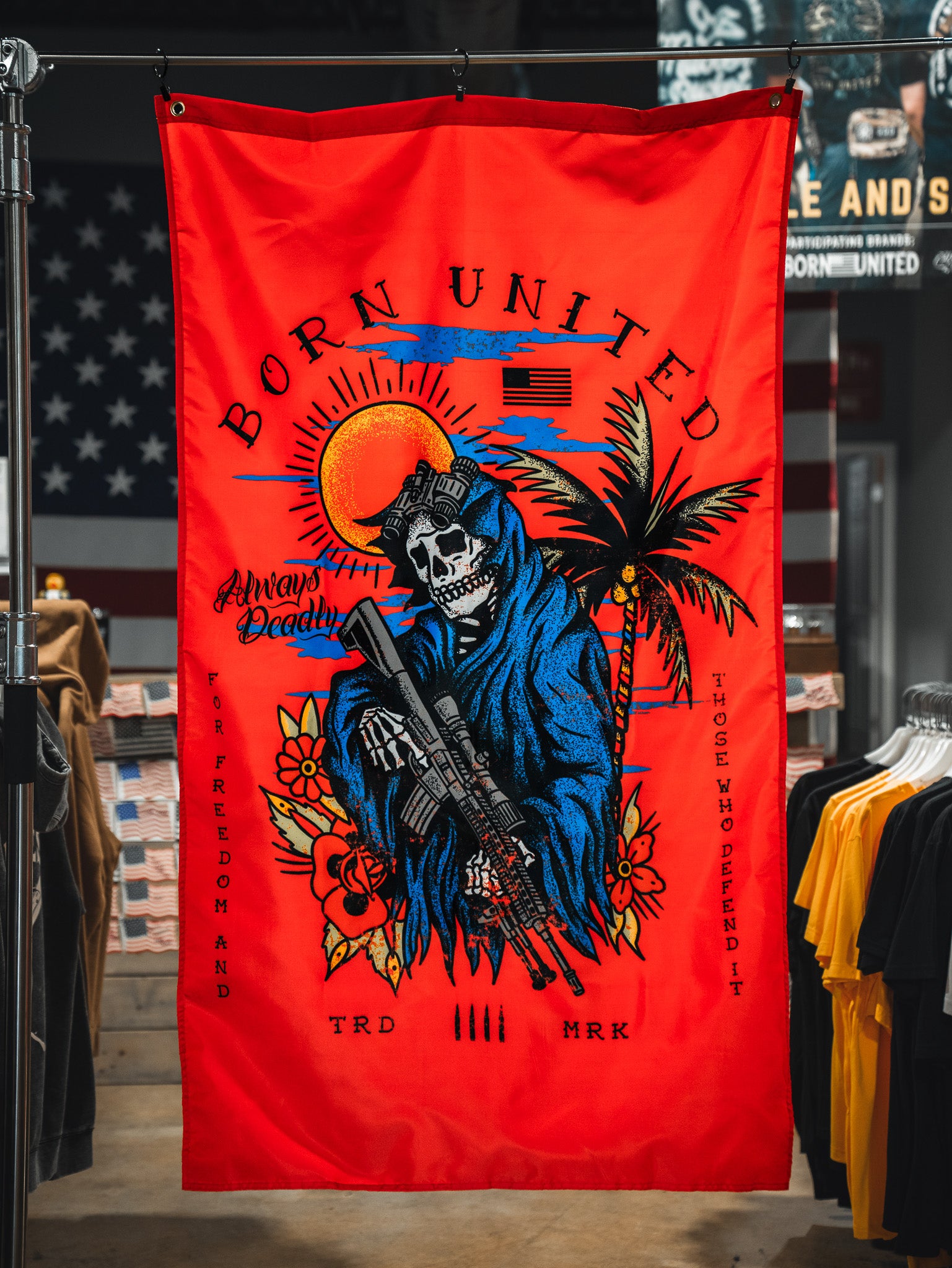The Always Deadly Flag by Born United Private Label features a grim reaper in a blue hood with a rifle on a red banner, plus sun, palm tree, and American flag accents. "Born United" and "Always Deadly" highlight its patriotic military design.