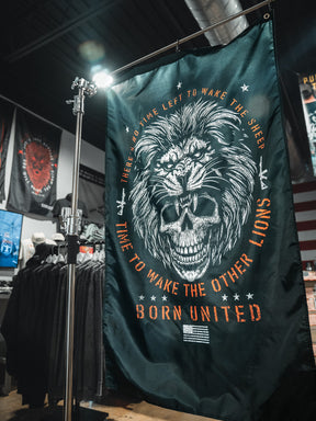The Waking Lions Flag by Born United Private Label, crafted from durable polyester, shows a roaring lion merged with a skull and reads: "There's no time left to wake the sheep. Time to wake the other lions. Born United." Ideal for indoor display.