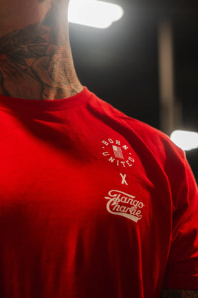 Close-up of a person in a red Make America Fit Again - Tee by Tango Charlie Apparel. Neck tattoos are visible, and bright lights blur the background—highlighting a bold style that promotes health and wellness.