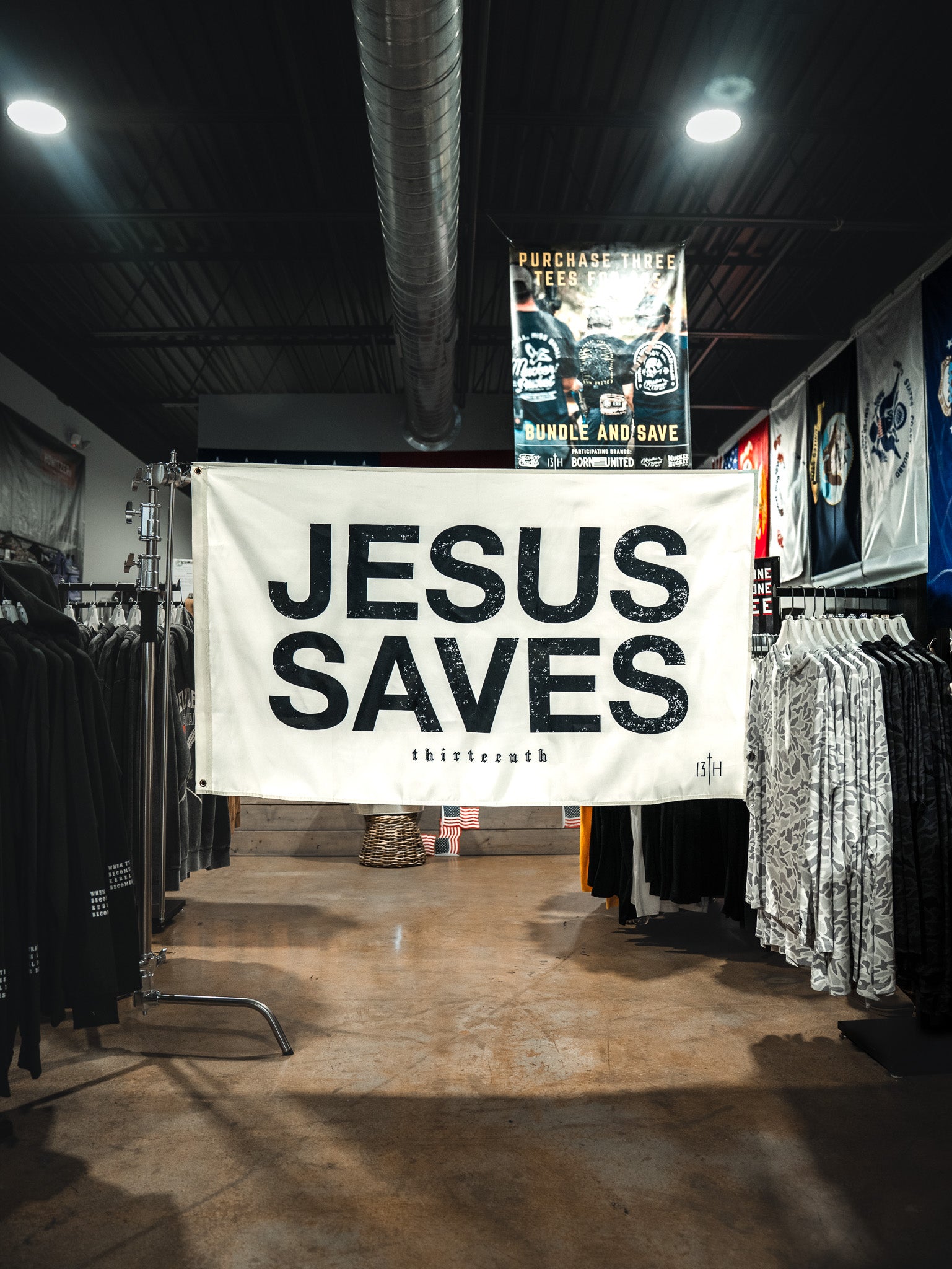 The 13th Jesus Saves Flag - Ivory hangs boldly in a clothing store, its striking black text standing out among racks of clothes and promotional signs for a powerful statement of faith.