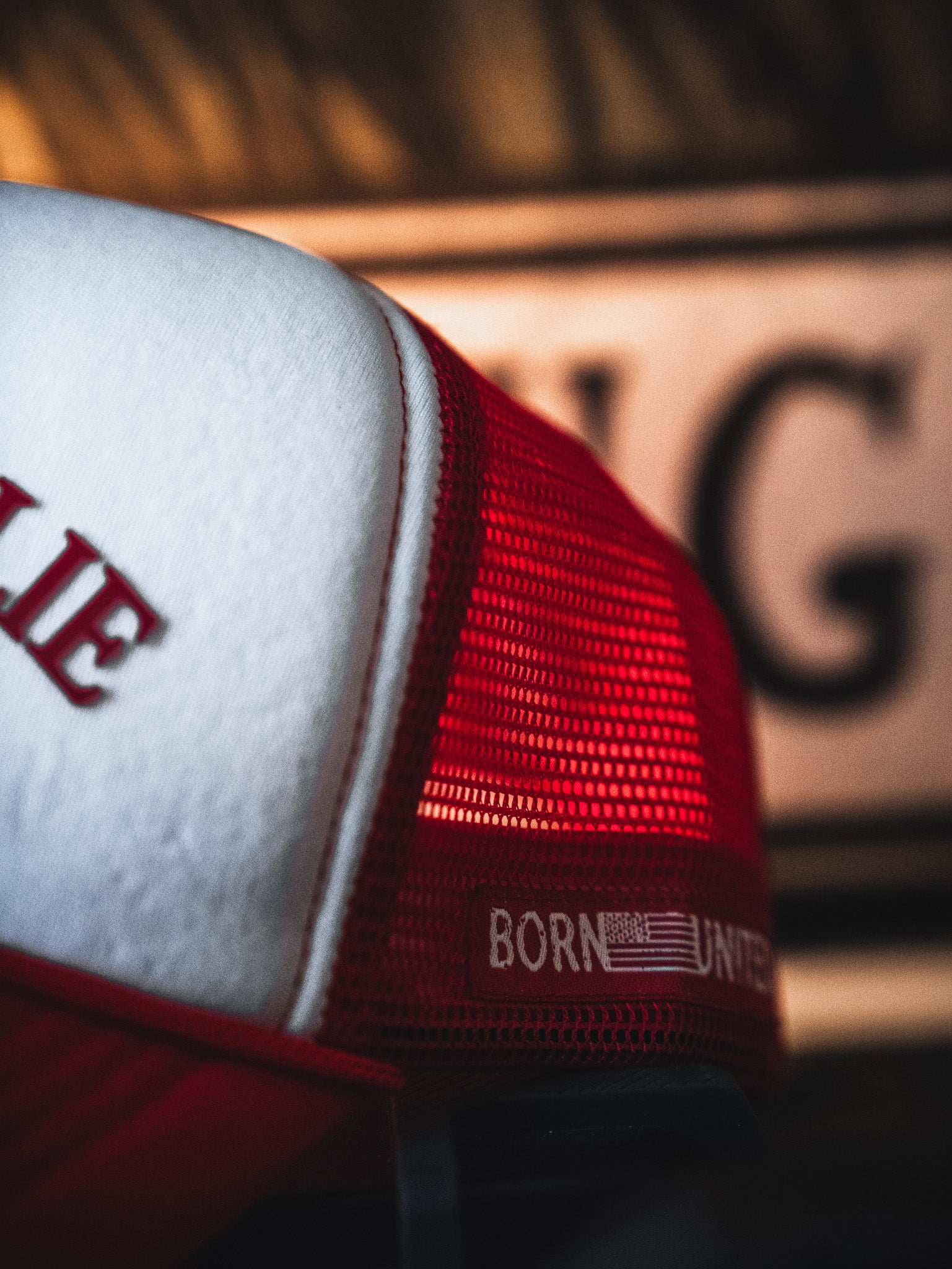 Close-up of the I Am Charlie Red Trucker Snapback by Born United Private Label. This 5-panel snapback features red and white mesh panels, a curved brim, and "Born United" embroidery beside a small American flag.