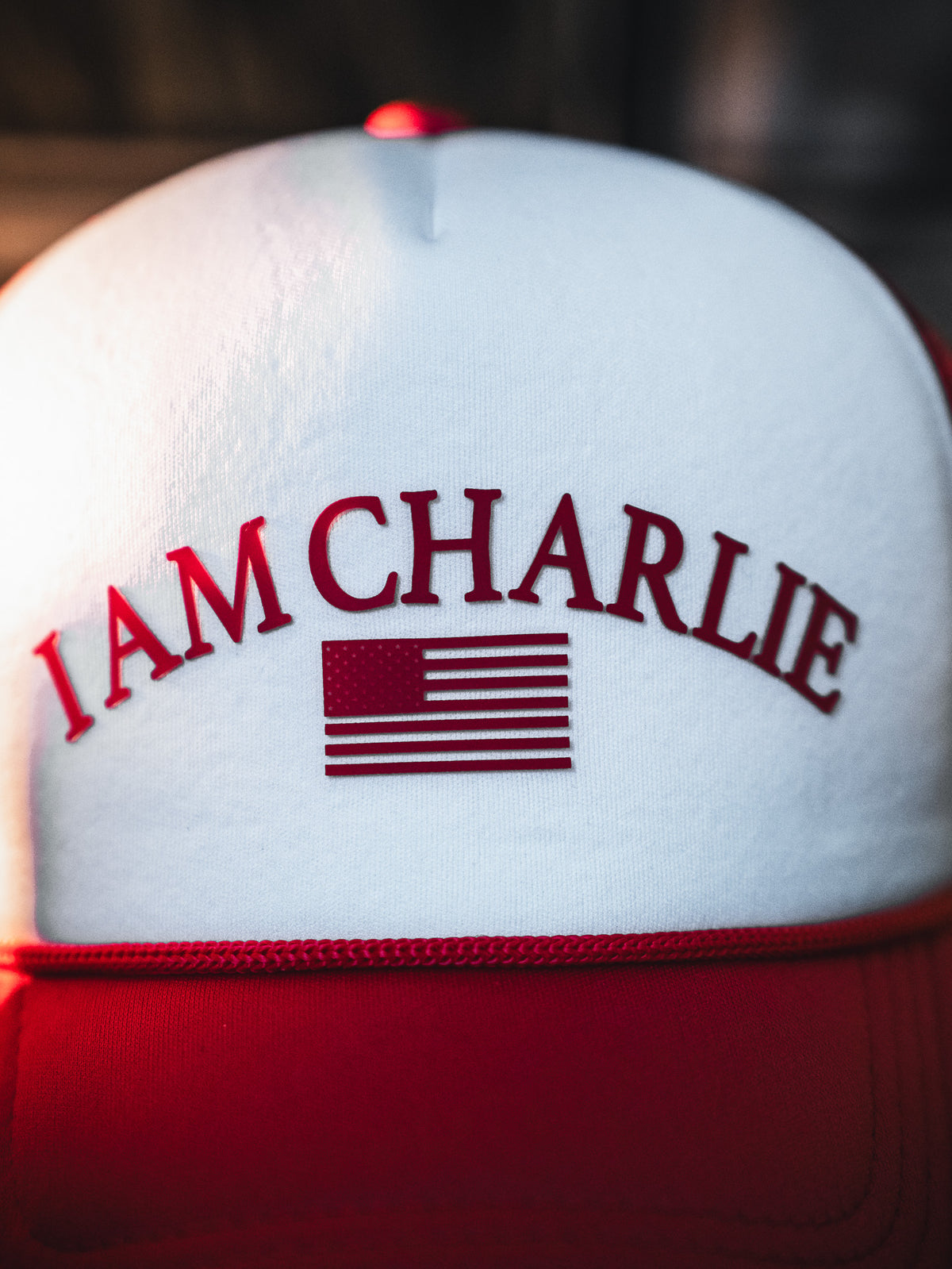 A close-up of the Born United Private Label "I Am Charlie Red Trucker Snapback," featuring "I AM CHARLIE" and an American flag in red on the white and red front.