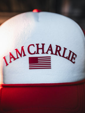 A close-up of the Born United Private Label "I Am Charlie Red Trucker Snapback," featuring "I AM CHARLIE" and an American flag in red on the white and red front.