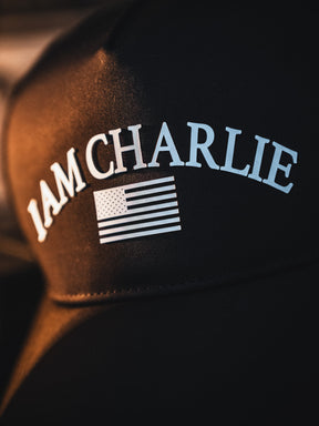 A close-up of the Born United Private Label I Am Charlie Black Snapback, a 5-panel curved bill cap with white "I AM CHARLIE" text above a stylized white American flag.