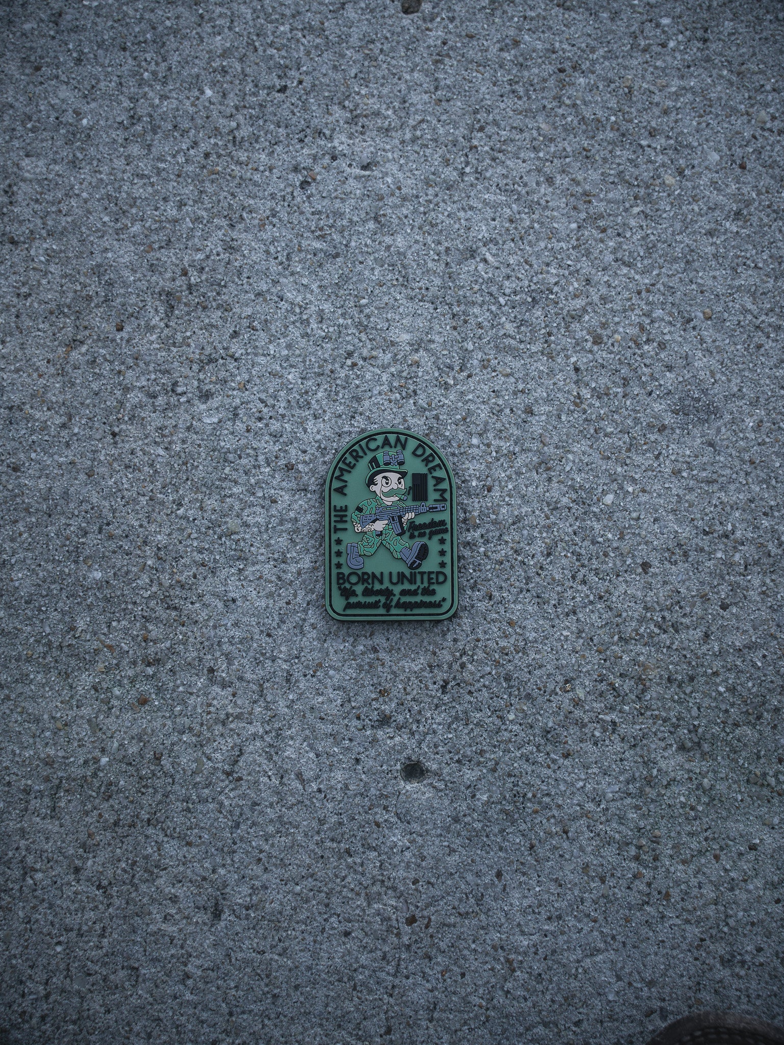 The American Dream PVC Patch by Born United Private Label, featuring an eagle logo and "The American Royal Born United, Quality Service" text, is displayed on a rough gray concrete surface.