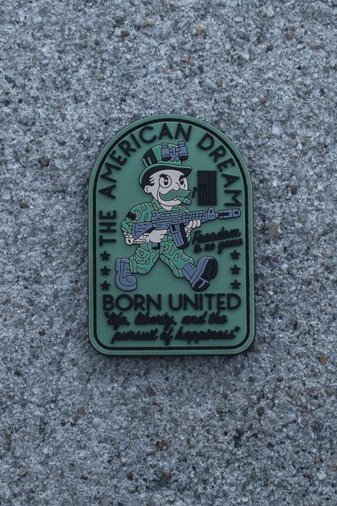 The American Dream PVC Patch by Born United Private Label features a cartoon soldier, rifle, and the text: “The American Dream—Born United—life, liberty, and the pursuit of happiness” plus “freedom isn’t free.” Perfect for collectors.