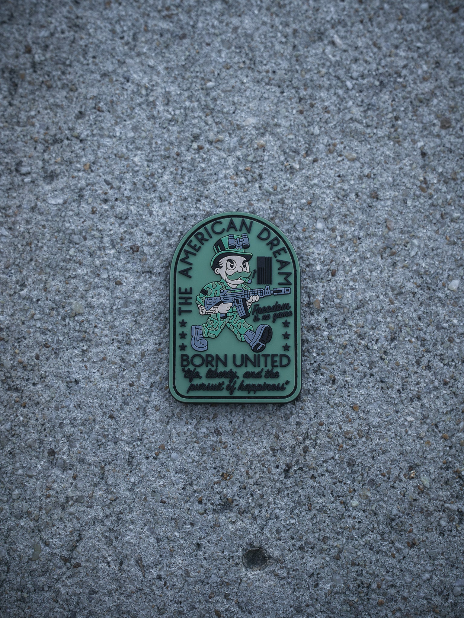 The American Dream PVC Patch by Born United Private Label features a cartoon soldier with a gun and cash, labeled "THE AMERICAN DREAM," with the text below: "Born United, Proudly served, pursued by happiness.