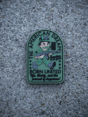 The American Dream PVC Patch by Born United Private Label displays a cartoon soldier with a rifle on a gray background, with "The American Dream, Born United, life, liberty, and the pursuit of happiness" plus stars and a flag.