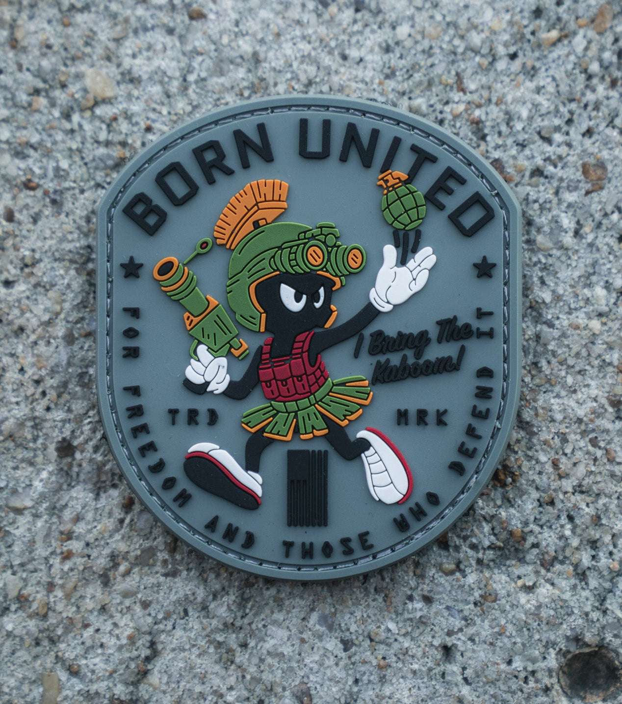 The Kaboom! PVC Patch by Born United Private Label shows Marvin the Martian in military gear with a grenade, "BORN UNITED" at the top, and "For freedom and those who defend" at the bottom, set on a textured concrete background.