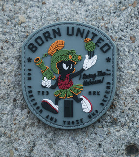 The Kaboom! PVC Patch by Born United Private Label shows Marvin the Martian in military gear with a grenade, "BORN UNITED" at the top, and "For freedom and those who defend" at the bottom, set on a textured concrete background.