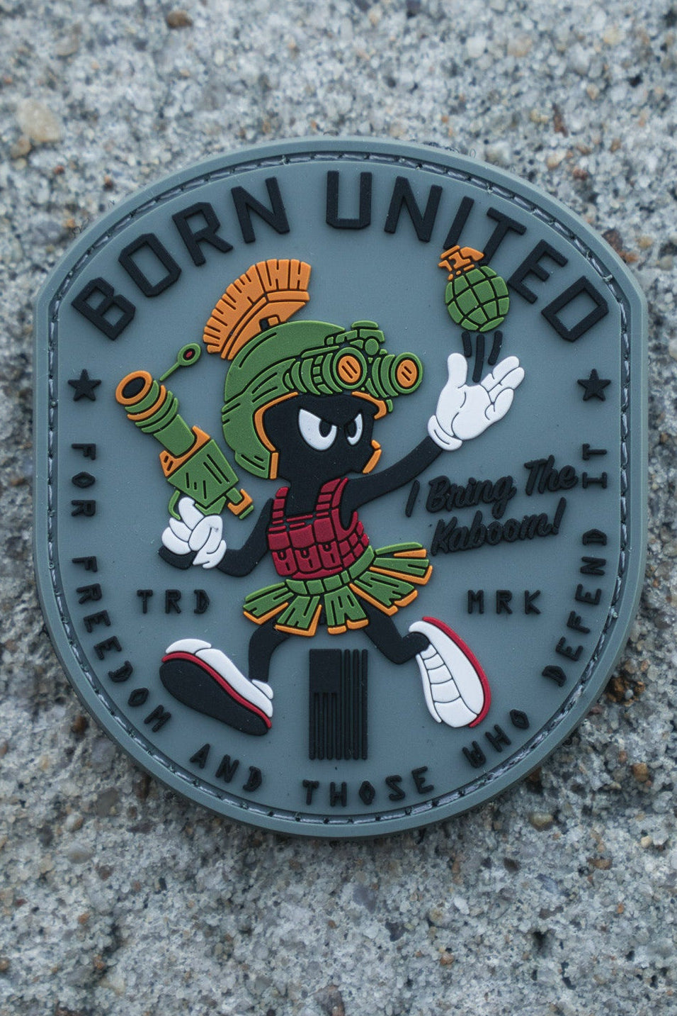 The Kaboom! PVC Patch by Born United Private Label shows Marvin the Martian in military gear with a grenade, "BORN UNITED" at the top, and "For freedom and those who defend" at the bottom, set on a textured concrete background.