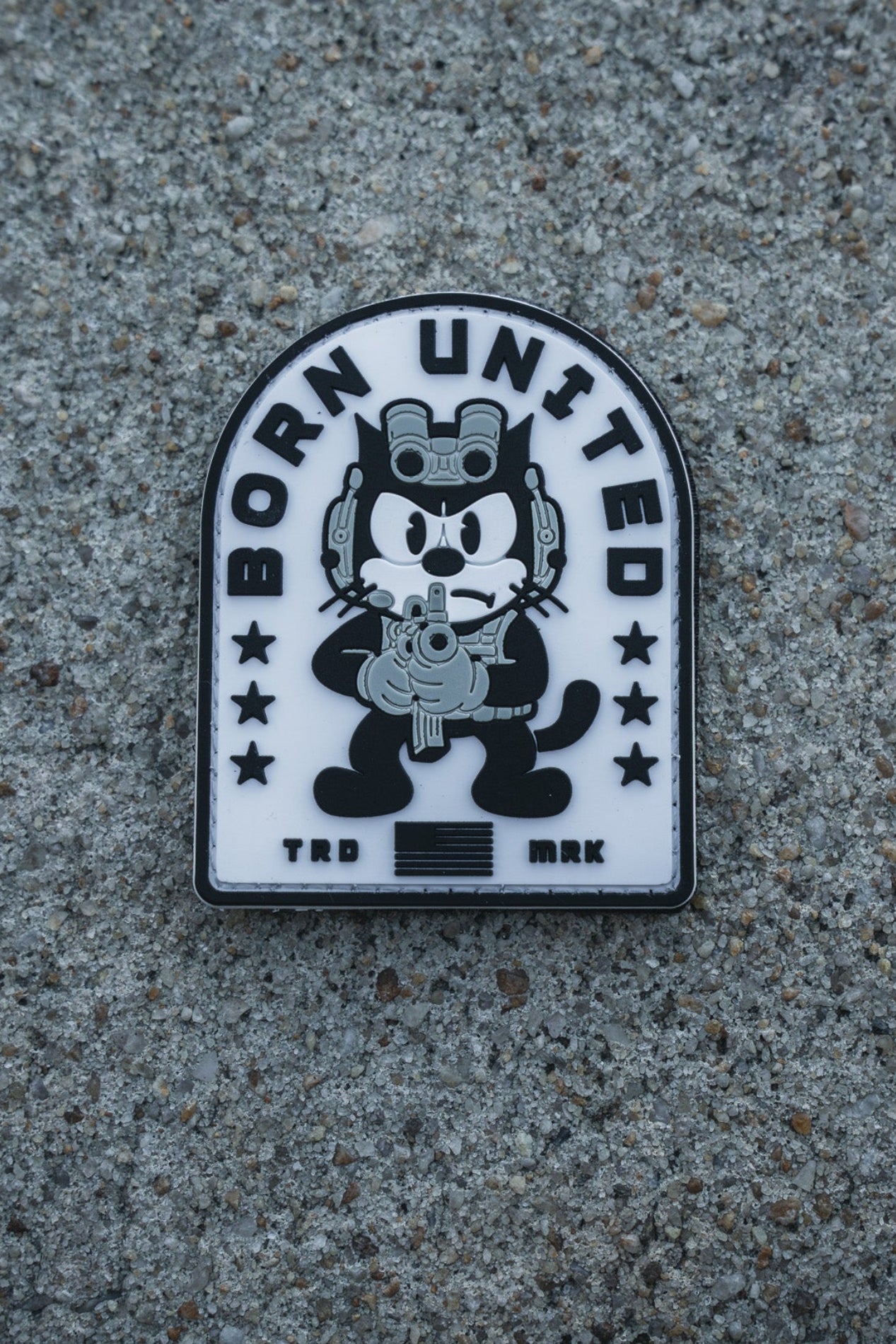 The Foxtrot Felix PVC Patch by Born United Private Label shows a cartoon cat in tactical gear with a rifle, "BORN UNITED" above, and "TRD MRK" below, set against a rough concrete surface.