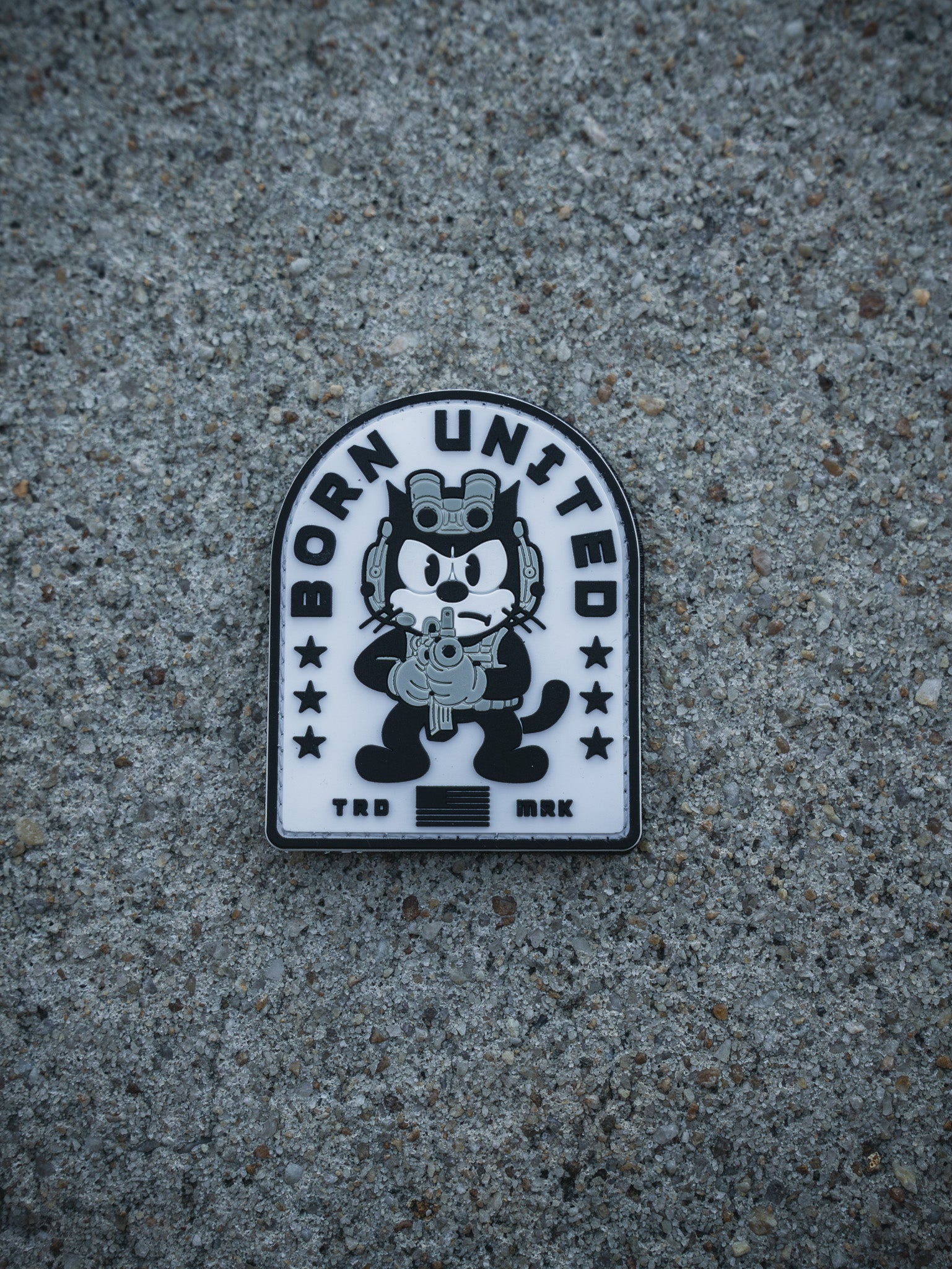 The Foxtrot Felix PVC Patch by Born United Private Label shows a cartoon cat in tactical gear with a rifle, "BORN UNITED" above, and "TRD MRK" below, set against a rough concrete surface.