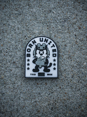 The Foxtrot Felix PVC Patch by Born United Private Label shows a cartoon cat in tactical gear with a rifle, "BORN UNITED" above, and "TRD MRK" below, set against a rough concrete surface.