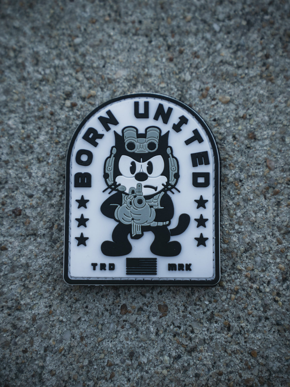 The Foxtrot Felix PVC Patch by Born United Private Label shows a cartoon black cat with night-vision goggles and rifle, "BORN UNITED" above, stars, stripes, and "TRD MRK" below—all on a textured gray background.