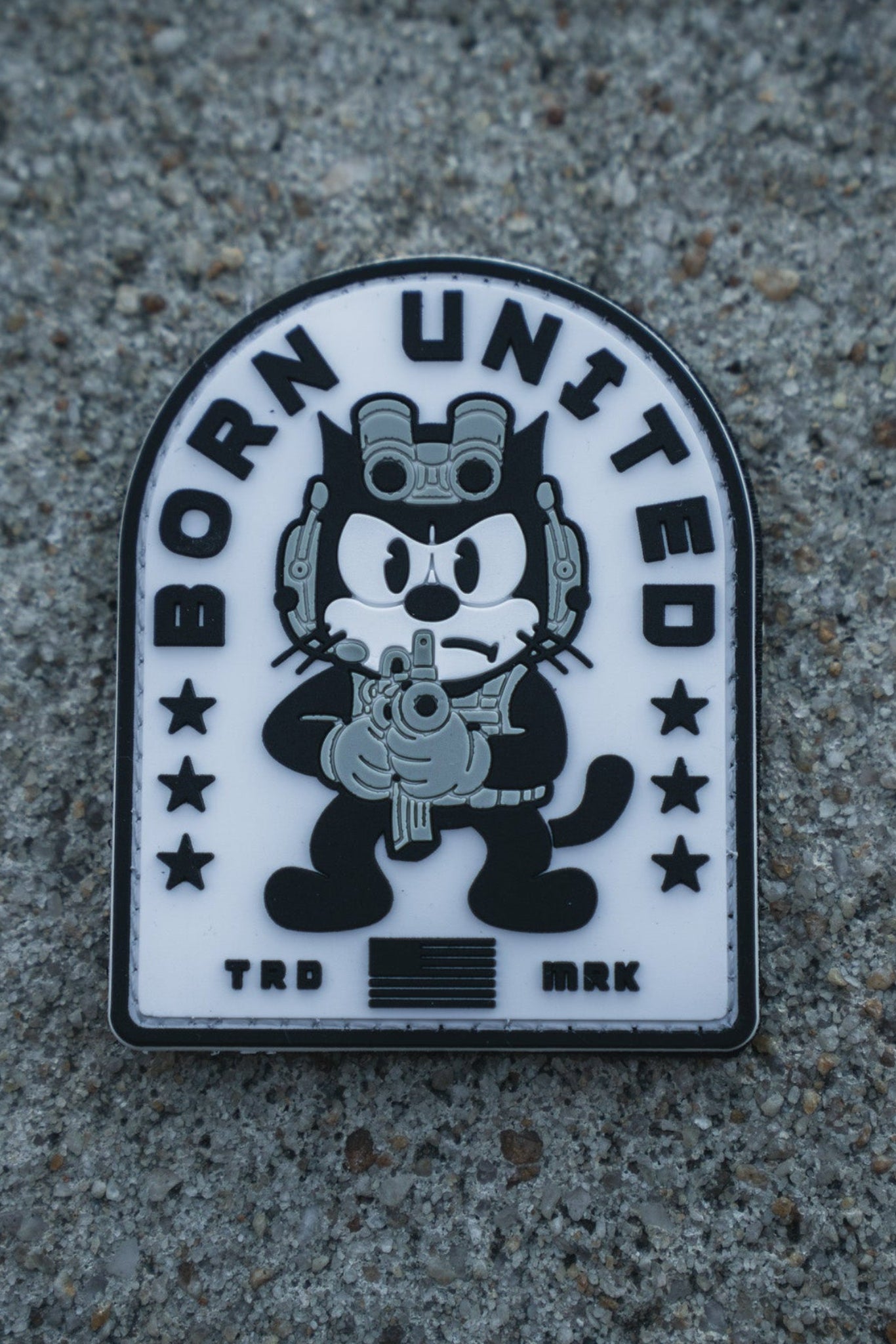 The Foxtrot Felix PVC Patch by Born United Private Label shows a cartoon black cat with night-vision goggles and rifle, "BORN UNITED" above, stars, stripes, and "TRD MRK" below—all on a textured gray background.