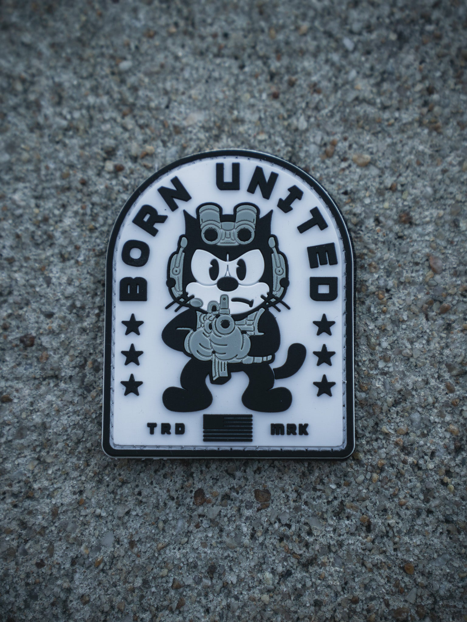 The Foxtrot Felix PVC Patch by Born United Private Label shows a cartoon black cat with night-vision goggles and rifle, "BORN UNITED" above, stars, stripes, and "TRD MRK" below—all on a textured gray background.