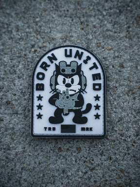 The Foxtrot Felix PVC Patch by Born United Private Label shows a cartoon black cat with night-vision goggles and rifle, "BORN UNITED" above, stars, stripes, and "TRD MRK" below—all on a textured gray background.