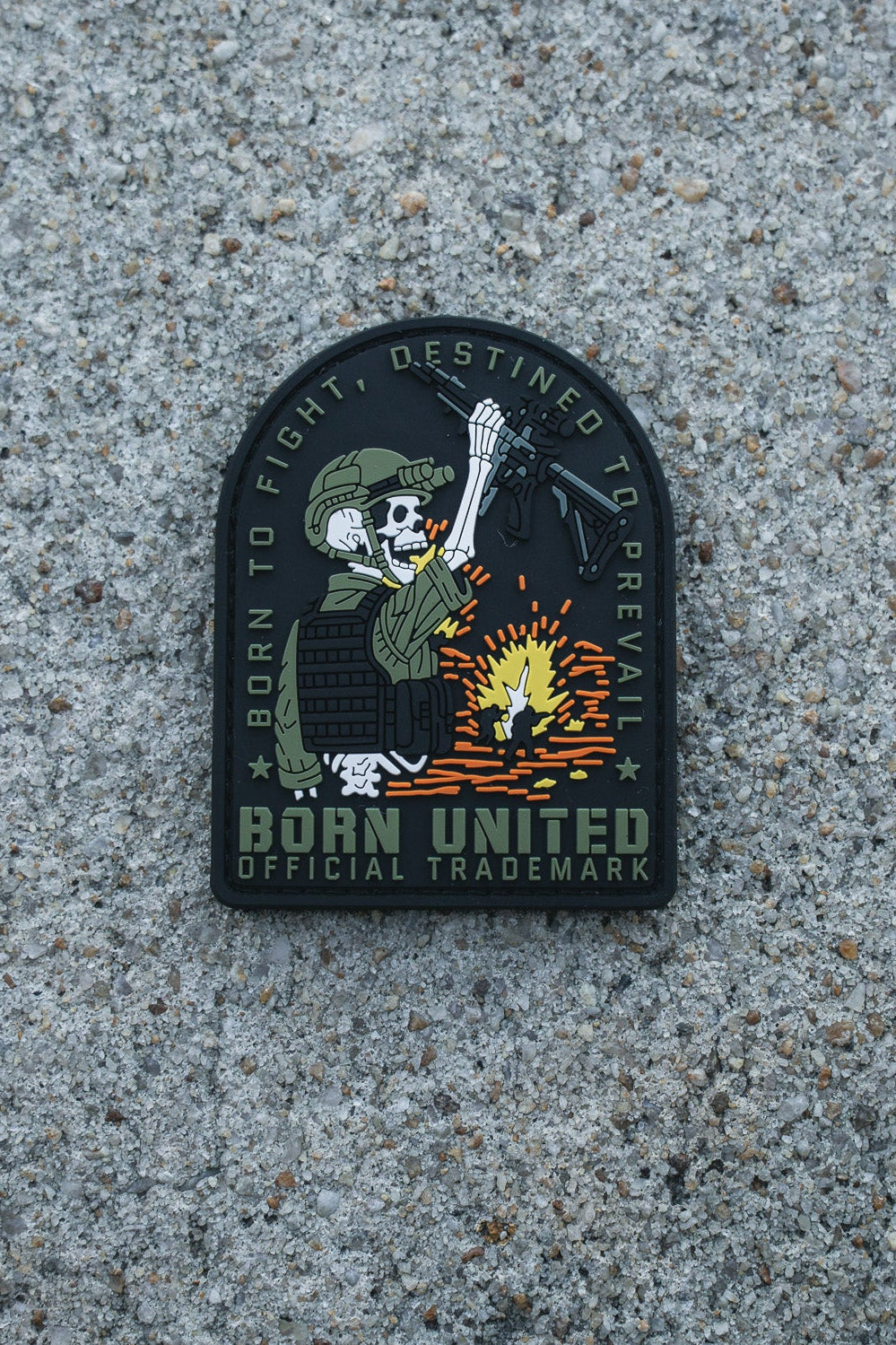 The Destined to Prevail PVC Patch by Born United Private Label features a skeleton in military gear with a rifle amid an explosion and the words “BORN TO FIGHT, DESTINED TO PREVAIL. BORN UNITED OFFICIAL TRADEMARK.” Ideal for tactical gear.
