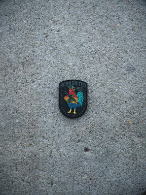 The Battle Bird PVC Patch by Born United Private Label features a colorful rooster and the words "BORN UNITED," "SOCCER," and "PHILADELPHIA" on a gray, textured concrete surface.