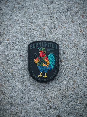 The Battle Bird PVC Patch by Born United Private Label shows a vibrant rooster in a helmet with a rifle. It reads "BORN UNITED" on top and "LOCKED, COCKED AND READY TO ROCK" below, all set against a rough concrete backdrop.